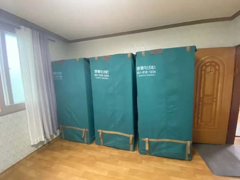 쌍용익스프레스 상호와 전화번호가 인쇄된 청록색 전용 포장 커버로 가구를 감싸 세워둔 모습
